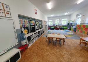 przestronna sala grupy piątej ze stolikami i krzesełkami dla dzieci, wyposażona w tablicę multimedialną