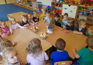 grupa dzieci przy stolikach ogląda soskowirówkę i owoce pokrojone