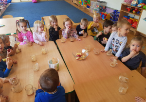 grupa dzieci przy stolikach ze szklankami z sokiem z owoców