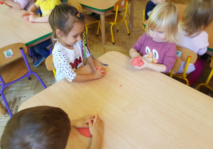 grupa dzieci przy stolikach lepi w rączkach czerwoną masę