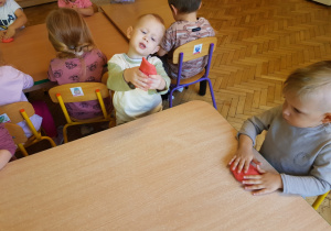 grupa dzieci przy stolikach lepi w rączkach czerwoną masę
