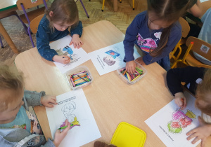 dzieci przy stolikach kolorują kartki z postaciami