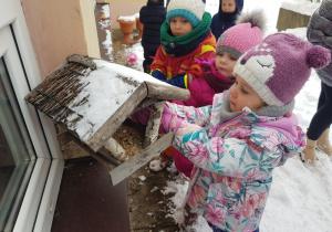 dzieci zgromadzone przy karmniku dla ptaszków sypią ziarenka