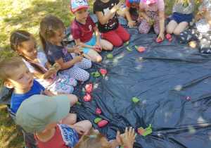 grupa dzieci ugniatajaca rękoma masy plastyczne na trawniku w ogródku