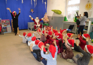 grupa dzieci w czerwonych swiątecznych czapkach podczas występu dla Mikołaja