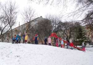 grupa dzieci na ośnieżonej górce w ogrodzie