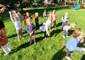 Grupa dzieci stoi na trawie i tańczy
