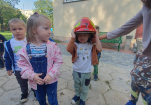 Grupa dzieci jedno dziecko przymierza hełm strażacki