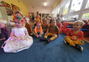 Grupa dzieci przebrane w stroje jesienne siedzą na dywanie