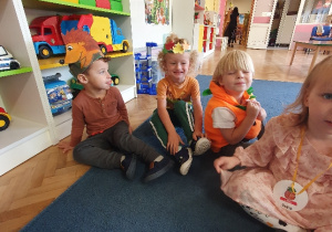 Grupa dzieci przebrane w stroje jesienne siedzą na dywanie