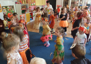 Grupa dzieci przebrane w stroje jesienne tańczą na dywanie