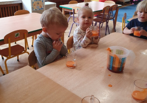 Dzieci siedzą przy stoliku piją sok marchewkowy