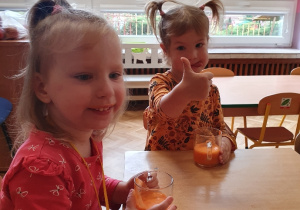Dwie dziewczynki siedzą przy stoliku trzymają w ręku kubek z sokiem