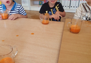 Chłopcy siedzą przy stoliku przed nimi stoją szklanki z marchewkowym sokiem