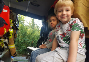 dzieci siedzące w szoferce wozu strazackiego