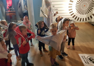 grupa dzieci w sali Muzeum trzyma chusty na głowę