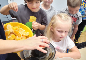 dzieci przy stolikach przygotowują owoce do sokowirówki