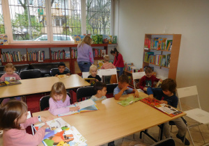 dzieci siedzące przy stoląch w bibliotece oglądające książeczki