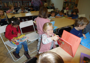 dzieci siedzące przy stoląch w bibliotece oglądające książeczki