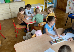 dzieci przy stolikach kolorują misia