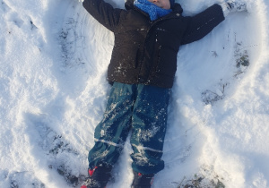 Dziecko leży na śniegu z wyciągniętymi na boki rękoma i nogami