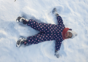 Dziecko leży na śniegu z rozciągniętymi na boki rękoma i nogami