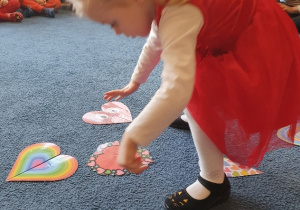 dziewczynka w czerrwonej sukience układa puzzle na dywanie