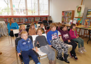 grupa dzieci siedzi na krzeslach przy regałach z książkami
