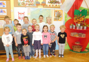 grupowe ustawienie dzieci na tle tablicy zawierającej informacje o Polsce