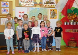 grupowe ustawienie dzieci na tle tablicy zawierającej informacje o Polsce