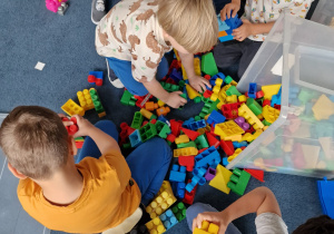 dzieci na dywanie buduja wspólnie z klocków