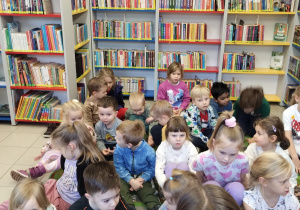 dzieci siedzą na dywanie w bibliotece na tle regałów z książkami