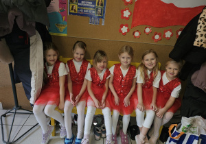 grupa dziewczynek ubranych na czerwono siedzi na ławce