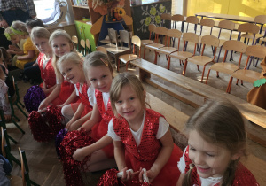 grupa dziewczynek ubranych na czerwono siedzi na ławce