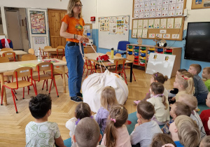 dzieci siedzą na dywanie przed kobietą mówiącą do nich