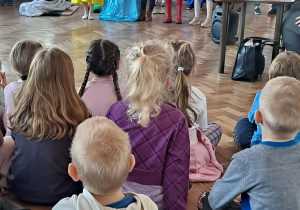 Grupa dzieci ogląda przedstawienie siedząc na podłodze.