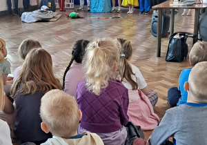 Grupa dzieci ogląda przedstawienie siedząc na podłodze.