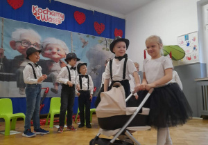 Dwójka dzieci prowadzi wózek, reszta dzieci stoi w tle