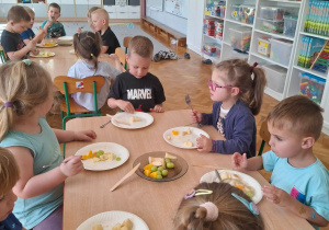 Dzieci przy stoliku kroją owoce do sałatki