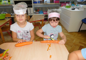 dzieci w czapkach kucharskich obierają marchew za pomocą skrobaków