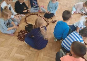 dzieci siedzą na podłodze i układają różne motywy z kasztanów