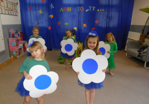 grupa dzieci na scenie z dużymi kwiatami papierowymi