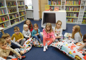 dzieci siedzące na kolorowych poduchach w sali bibliotecznej