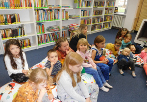 dzieci siedzące na kolorowych poduchach w sali bibliotecznej