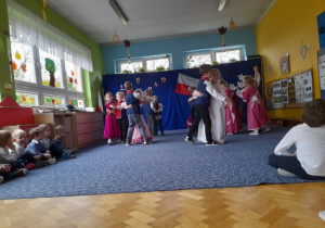 chłopcy ubrania w stroje ułanów i dziewczynki w długich sukniach odświętnyvh podcza tańca w sali