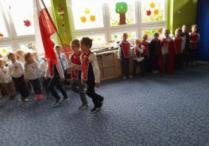 troje dzieci niosące flagę polski w sali podczas uroczystości