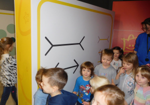 dzieci stojące przy dużym obrazie z narysowanymi liniami do porównania długości
