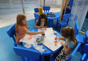 dzieci przy stolikach malujące farbami