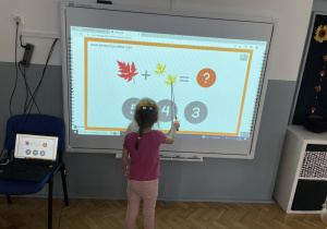 dziecko przesuwa wskaźnikiem wyświetlony element przy tablicy interaktywnej