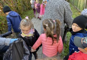 grupa dzieci w ogrodzie przedszkola zbiera śmieci do worka